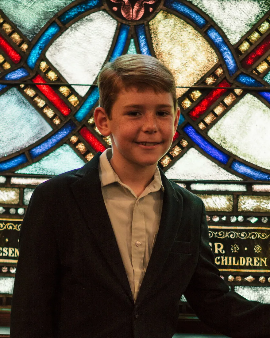 James Watson in a suit standing by the stained glass at church